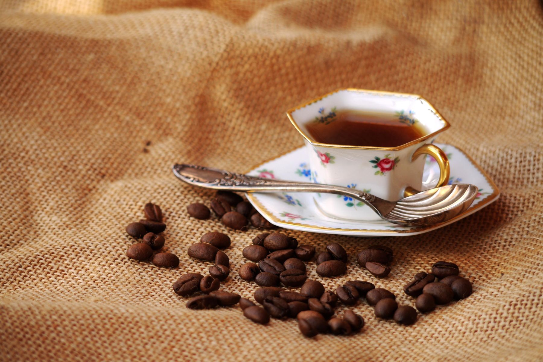 Alte Kaffetasse mit Kaffee darin und Bohnen davor auf einem Kaffeesack